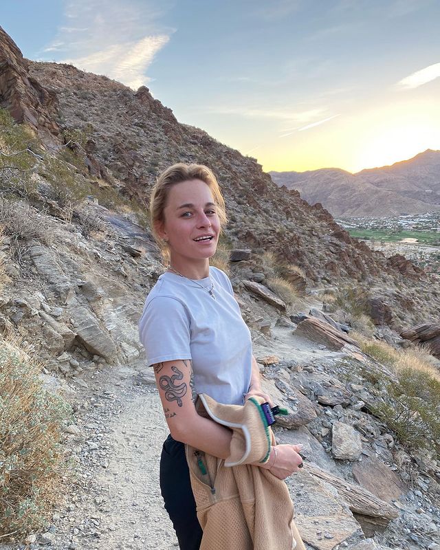 Ekaterina Gordeeva in a light blue t-shirt and black pants showing her tattoo.